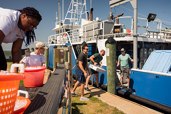 A group of people gathered on a dock, loadnig a watercraft and smiling.