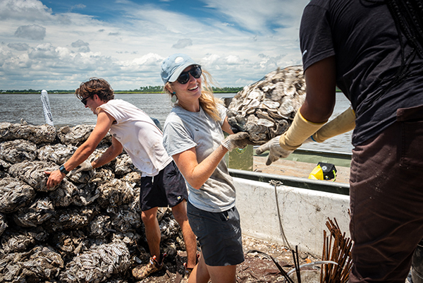 Oyster shells being passed from person to person from a large pile of oysters.