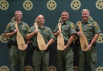 Lane Cpl. Matthew Owen, Pfc. Brain Hoover, Pfc. JP Cooler, Staff Sgt. Philip Robertson in SCDNR officer uniforms holding wooden Officer of the Year awards.