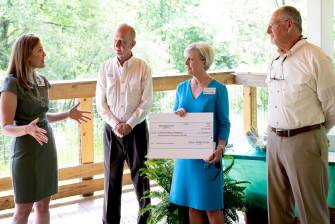 two women and two men chatting while one of the women is holding a large check