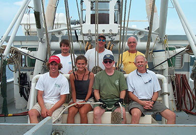 Group of people sitting on a vessel, smiling at the camera.