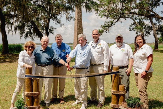 group photo of men and women cutting a ribbon with giant scissors