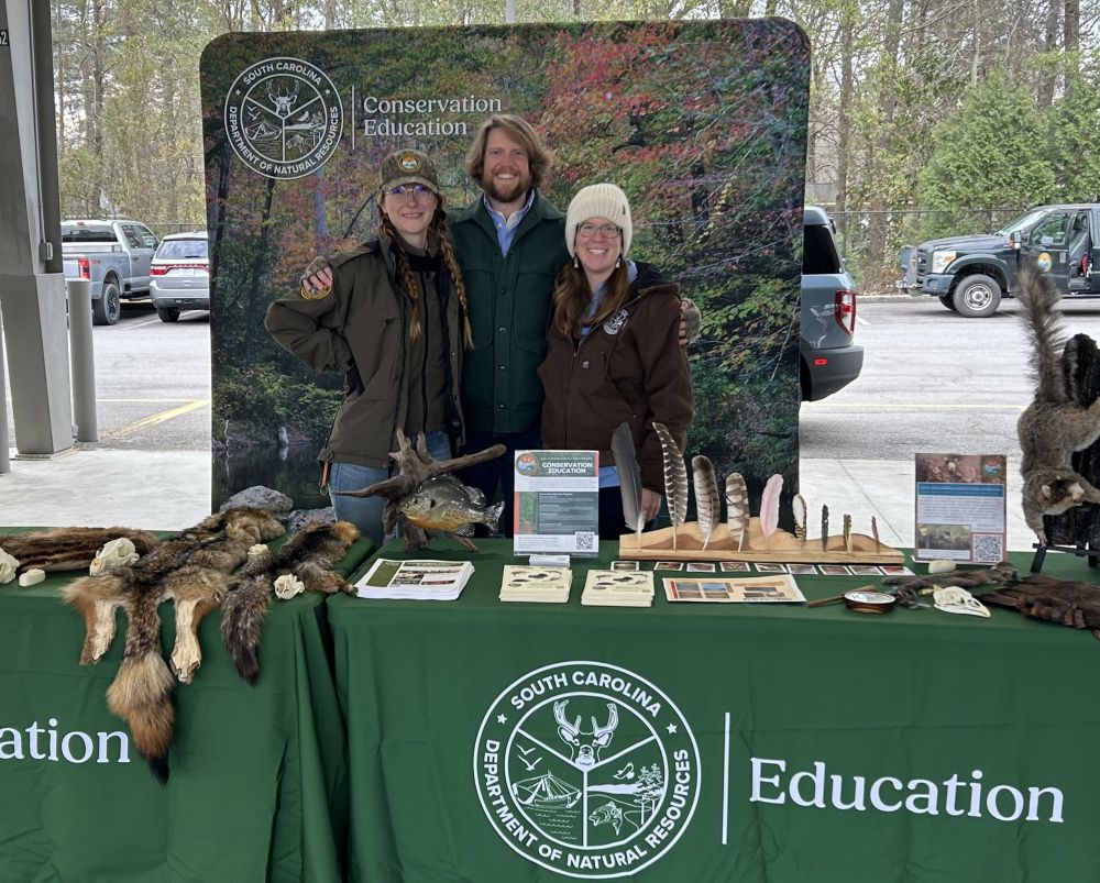 Three SCDNR employees standing in front of a table ready to talk about conservation education
