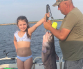 Smiling girl and man holding a blue catfish