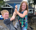 two smiling children holding a blue catfish