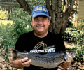 Smiling man in a hat holding a brown trout