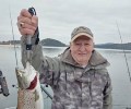 Smiling older man on a boat holding a brown trout forward