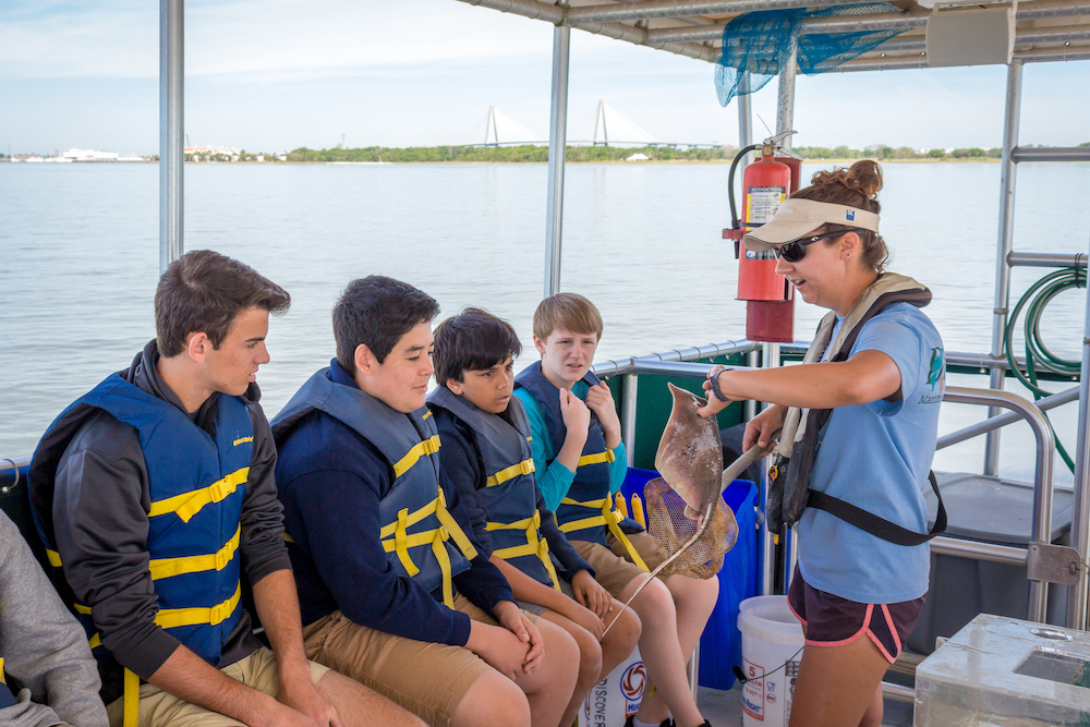 Students on an education boat cruise studying a male stingray pulled from the trawl net