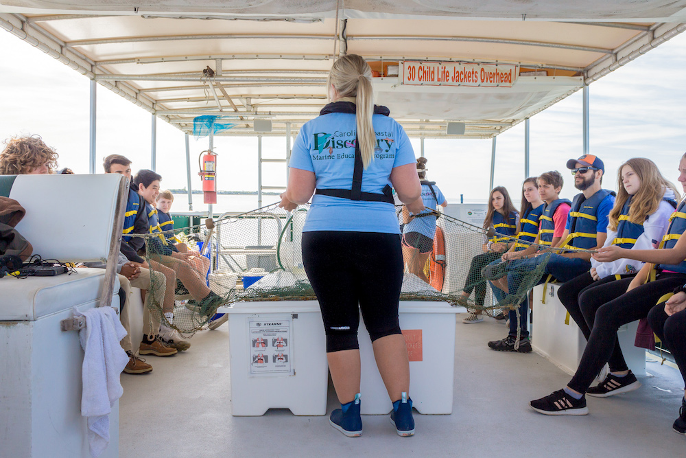 A class aboard the E/V Discovery holding a trawl net and learning how it functions